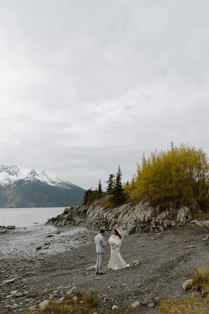 Bride and groom exchanging vows on a rocky beach along Turnagain Arm in Alaska on an overcast day.