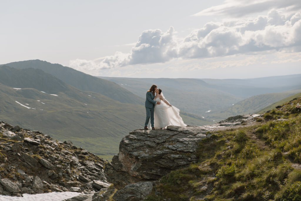 Bride and groom sharing a passionate kiss while embracing on a rocky overlook in Hatcher Pass, Alaska.