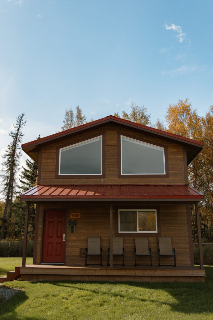 Front exterior of 'Pine' cabin with arched roof, two large upper windows, and red door, overlooking Palmer Valley mountains.