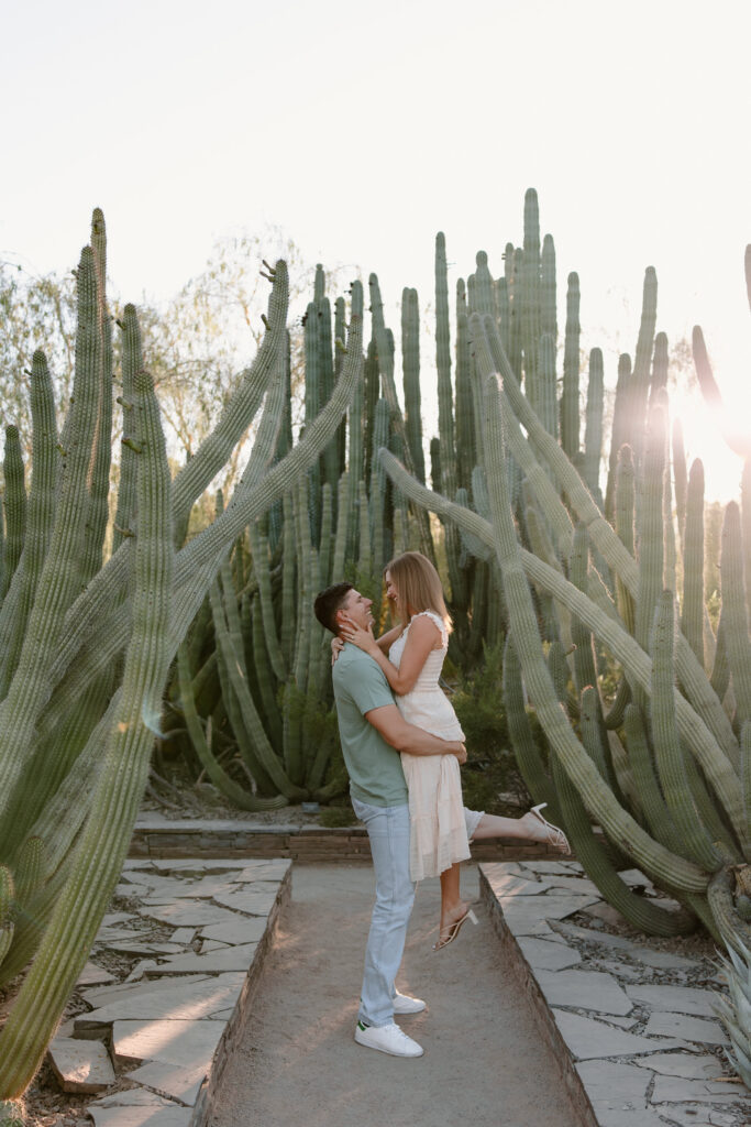Man picks up fiance as they smile at each other surrounded by cacti at the Phoenix Botanical Garden