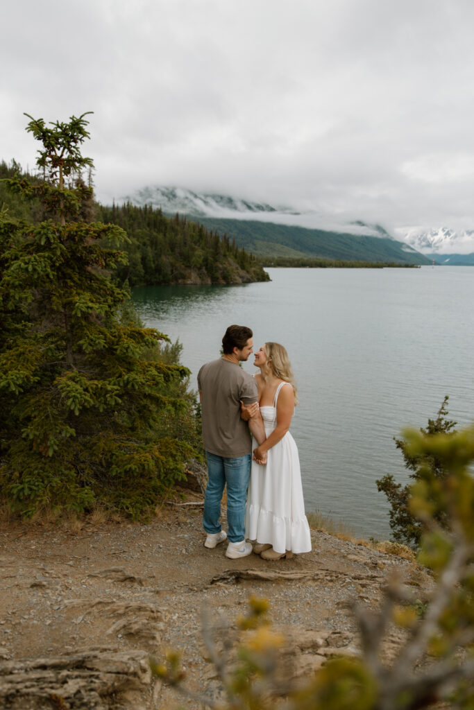 Engaged couple holding hands and gazing at each other at an overlook above Kenai Lake in Cooper Landing Alaska