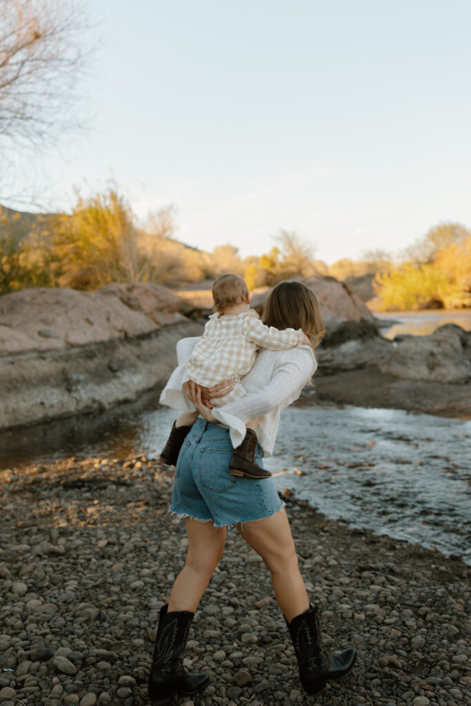 Mom carries daughter on her back as they walk towards a creek.