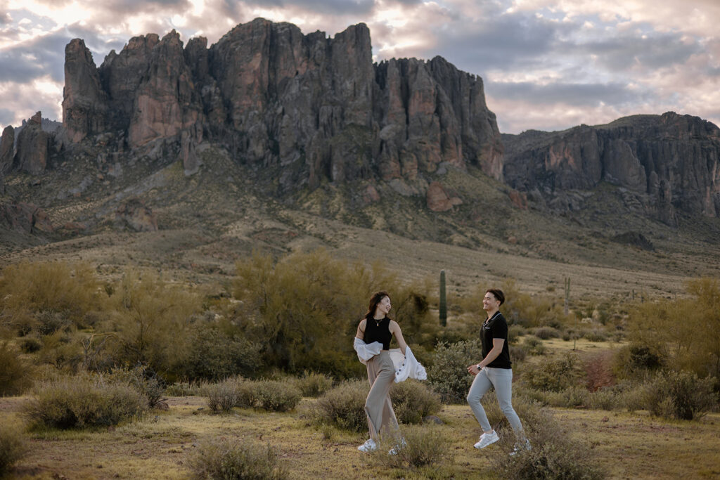 Couple runs after each other at Lost Dutchman State Park. Large mountain behind them.