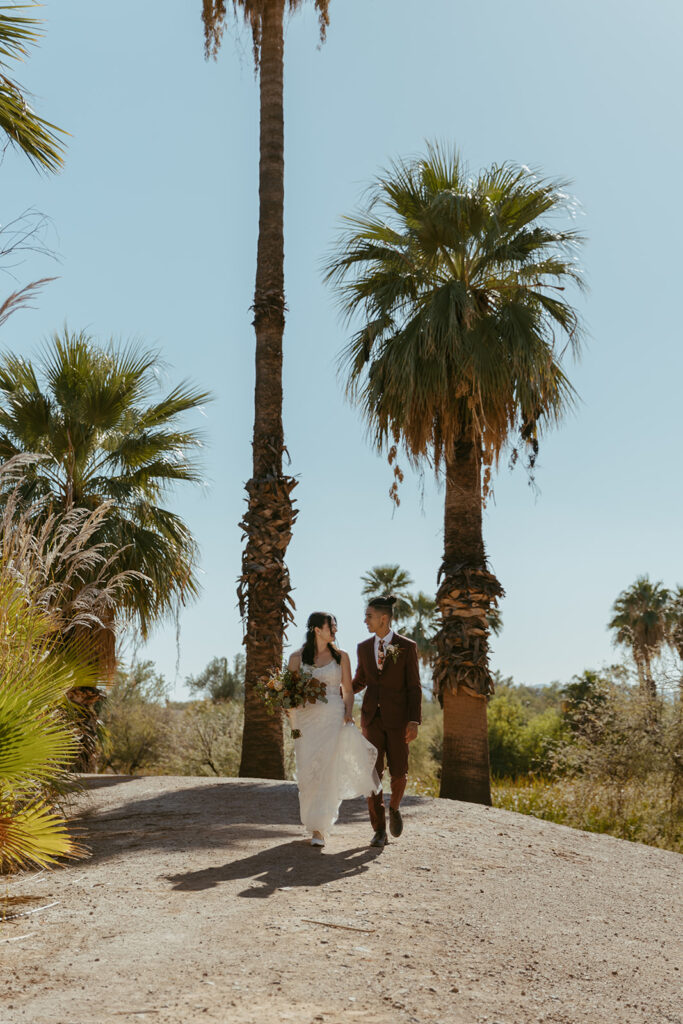 Wedding couple walks together down a hill on a sunny day. There is palm trees surrounding them.