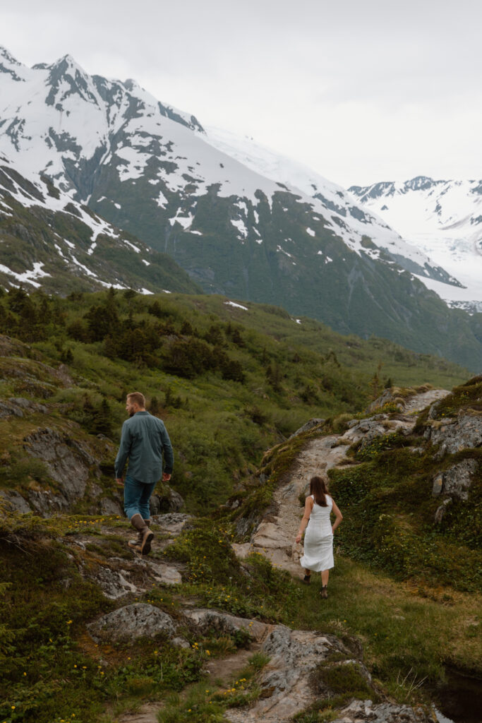 Engaged couple walking along the ridgeline at Portage Pass Alaska with snowy mountains in the distance