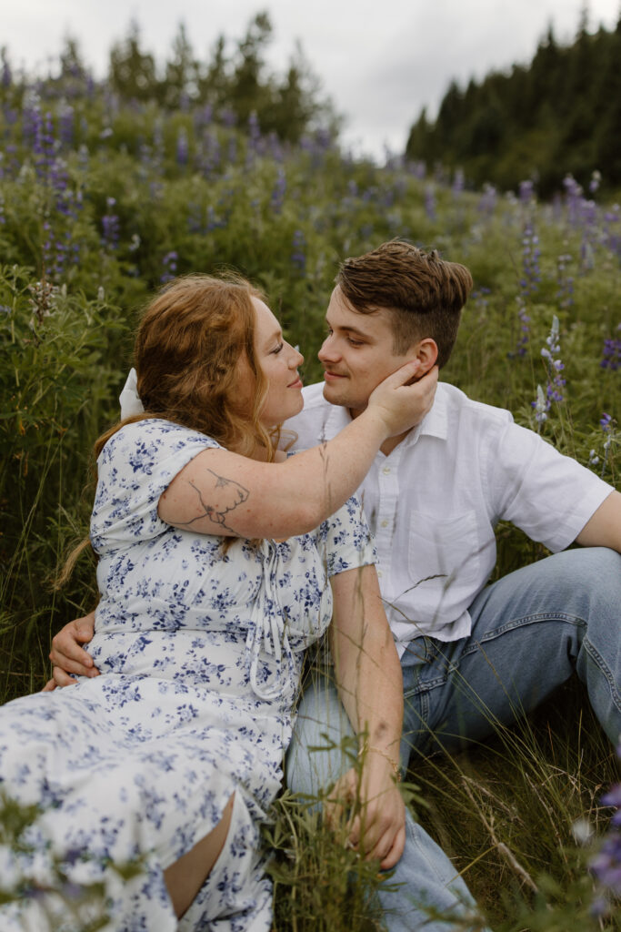 Couple sitting together in a wild lupine field outside Seward Alaska, girlfriend pulling boyfriend's face close to hers