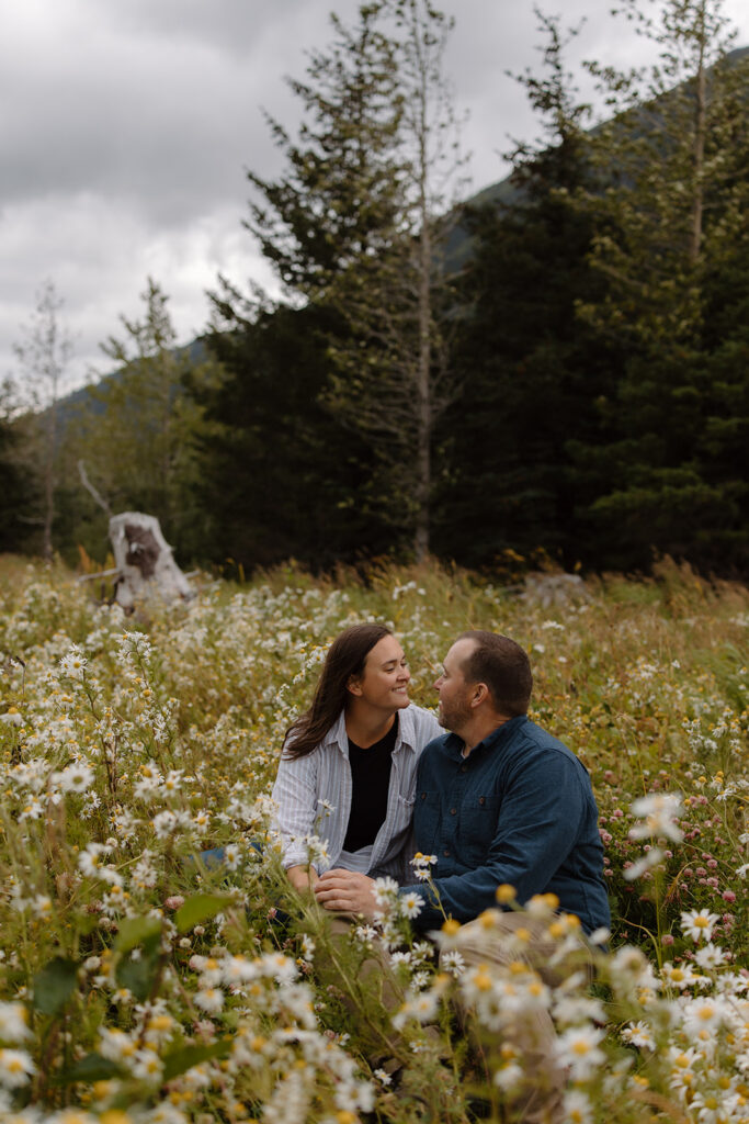 Married couple sitting together at Portage Alaska, bride smiling at each other with daisies surrounding them on an overcast day.