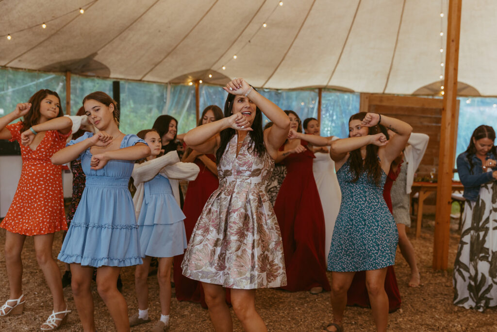 Wedding guests are dancing with their arms raised into the air. 