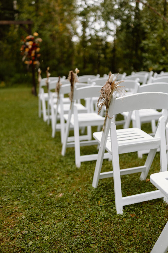 Close up view of white wedding chairs for guests to sit on. There is dried foliage attached to the chair for decoration.