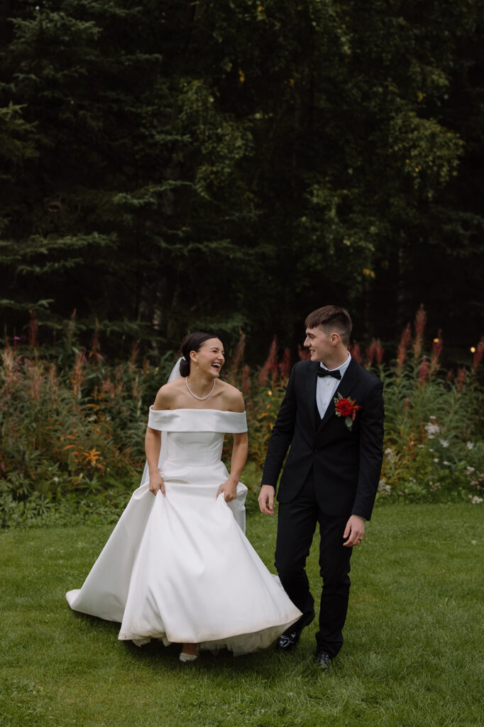 Bride and groom run forward and are laughing together, surrounded by a green forest and fireweed.