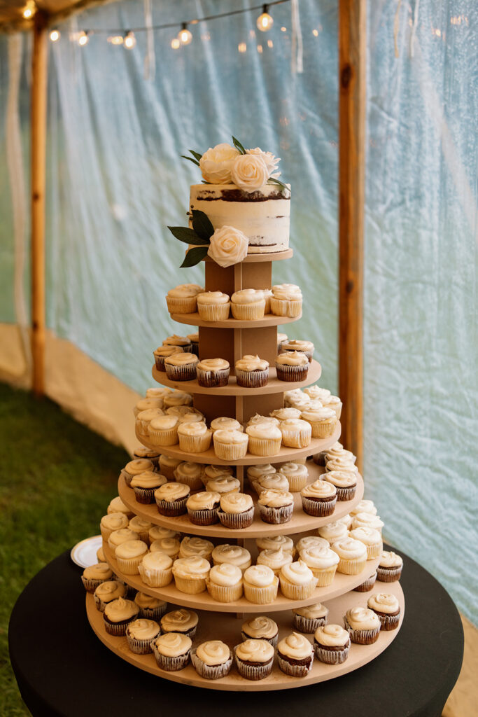 A tower of cupcakes with a small wedding cake at the top adorned with white roses.