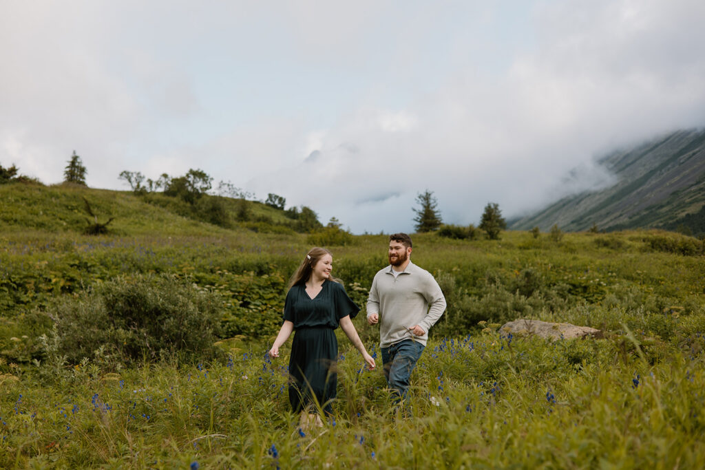 Engaged couple embracing in a green mountain valley in South Central Alaska, groom kissing bride on the cheek as she smiles