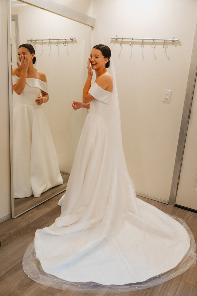 Bride pats away her happy tears and she stands in front of mirror and looks back at bridemaids.