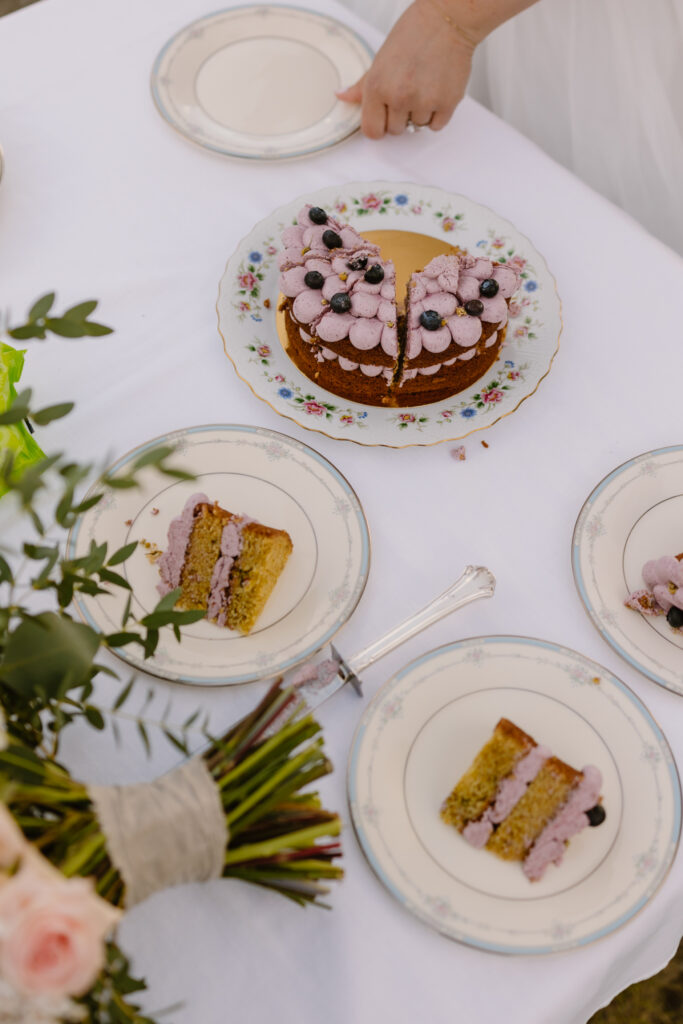 Wedding cake with purple frosting being cut during a Hatcher Pass elopement celebration with flower bouquet and plated slices ready to serve