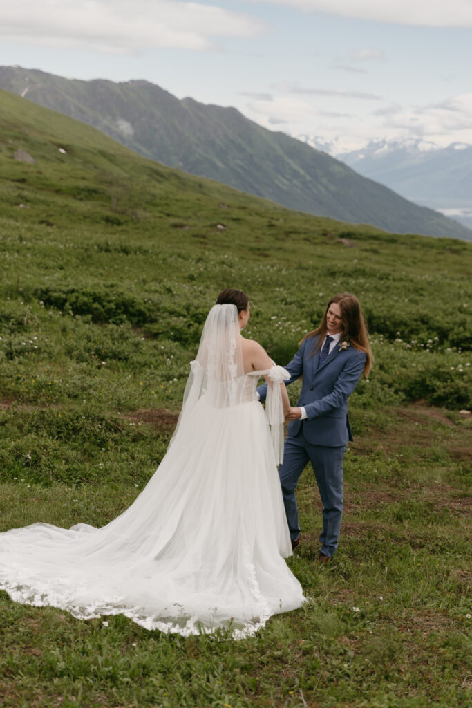 Grooms holds hands of bride smiling during their first look in Hatcher Pass Alaska.