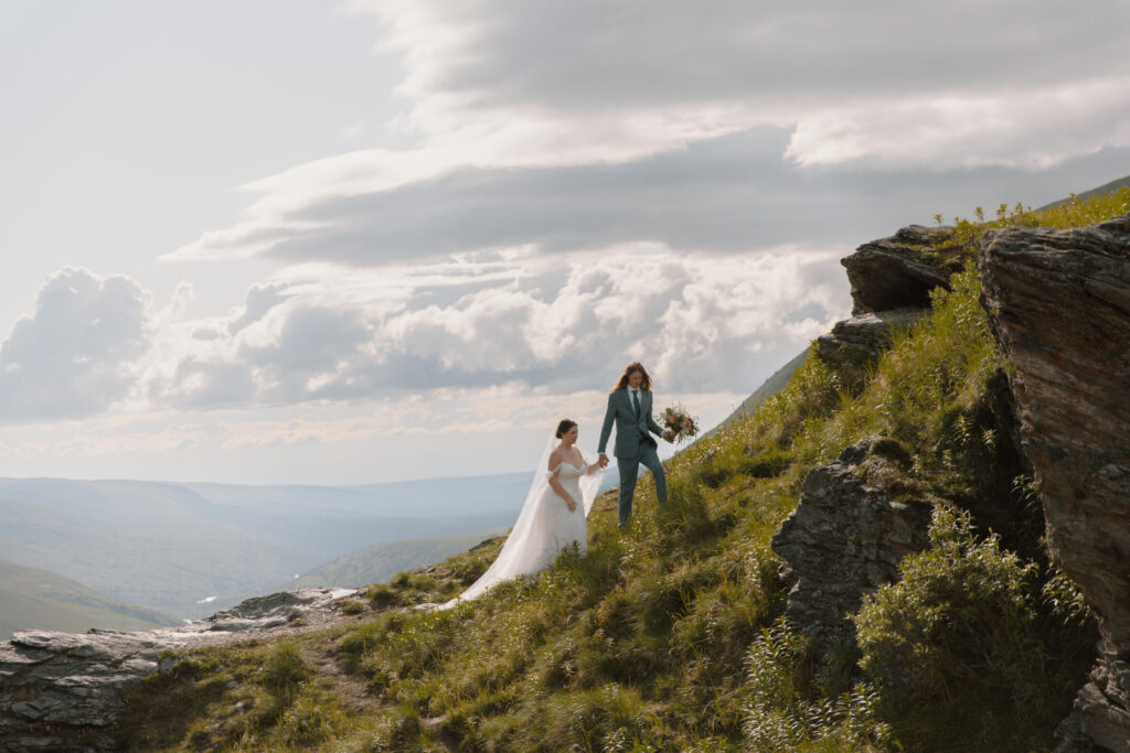 Groom leading bride up a grassy hill during their Hatcher Pass elopement in the Talkeetna Mountains Alaska