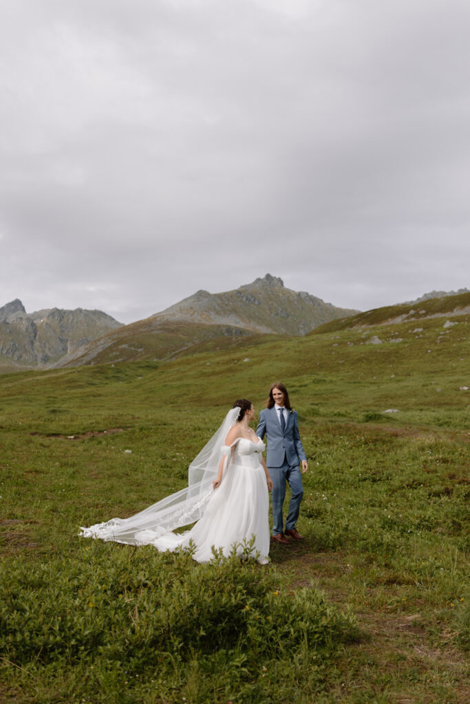 Bride and groom walking together through the alpine bowl during their Hatcher Pass elopement with mountain peaks surrounding them