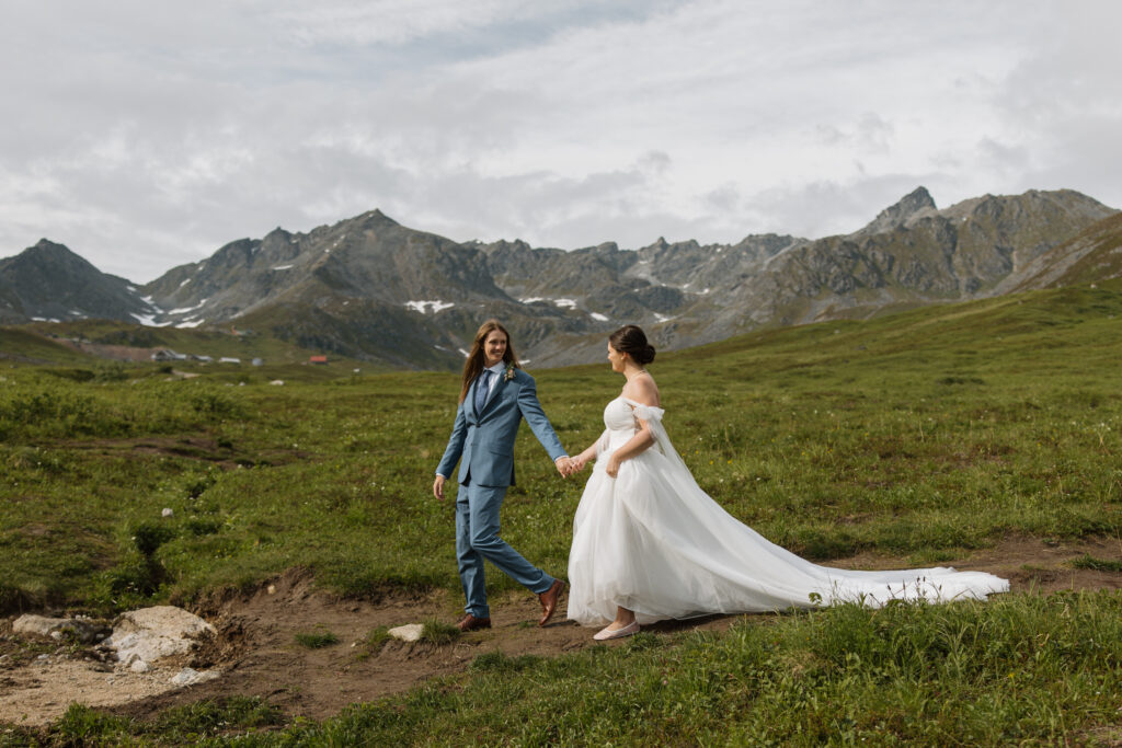 Bride and groom walking together through the alpine bowl during their Hatcher Pass elopement with mountain peaks surrounding them