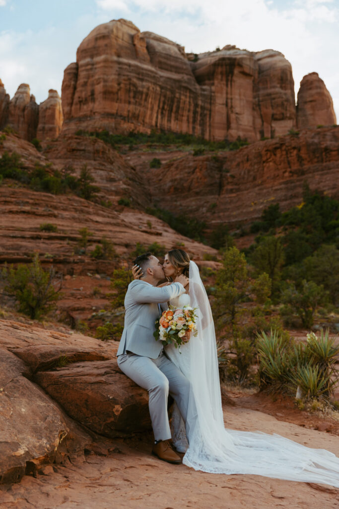 Bride kissing groom as he sits on a rock at Cathedral Rock trail during their Sedona Arizona elopement
