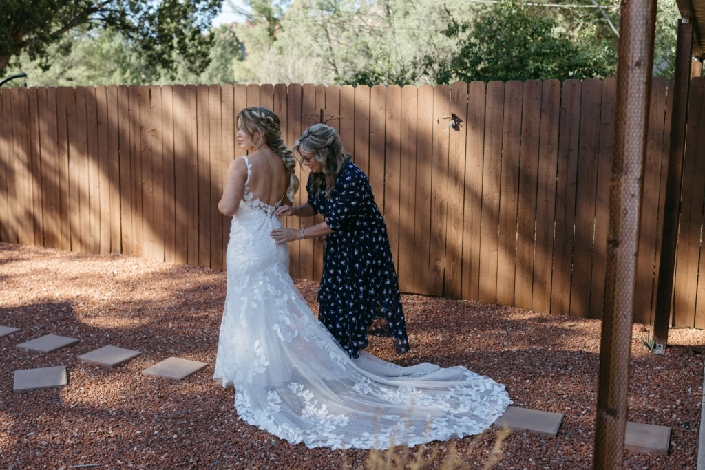 Mother helping bride button into her wedding dress in the backyard of a Sedona Arizona Airbnb on elopement morning