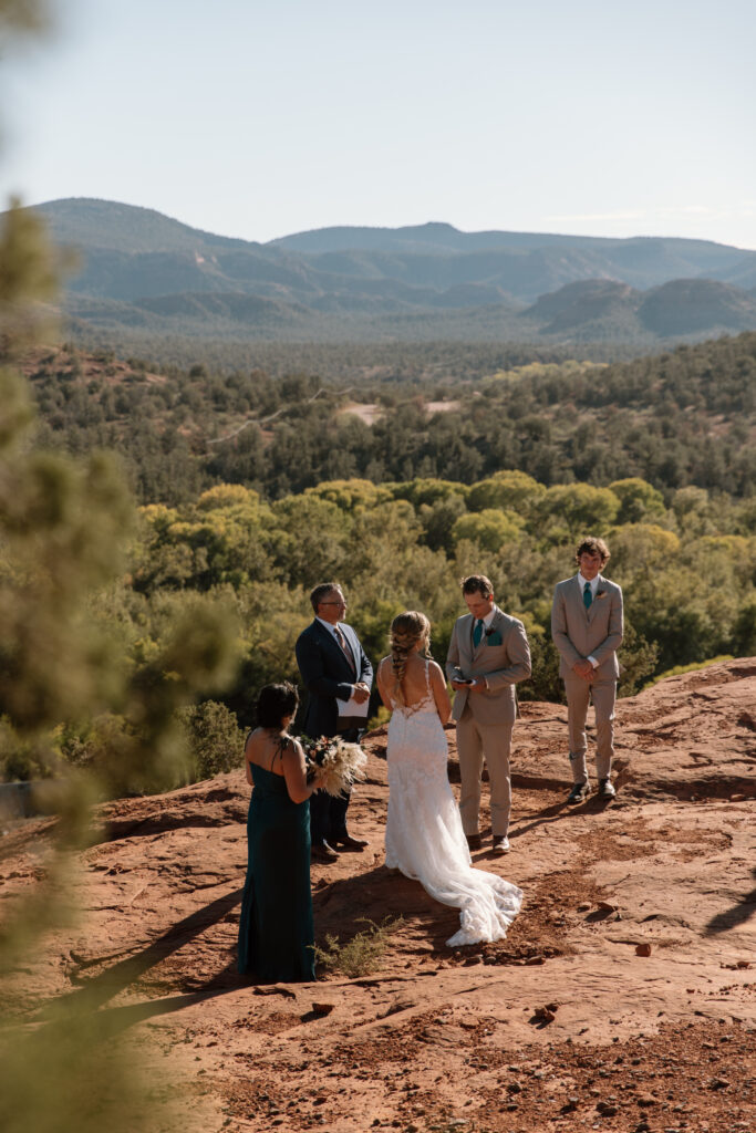 Guests watching the ceremony from a distance at a Secret Slickrock elopement in Sedona Arizona on a sunny day with rolling red rock hills in the background