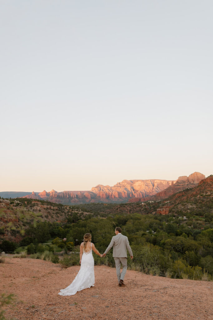 Bride and groom walking hand in hand toward the overlook during their Secret Slickrock elopement in Sedona Arizona