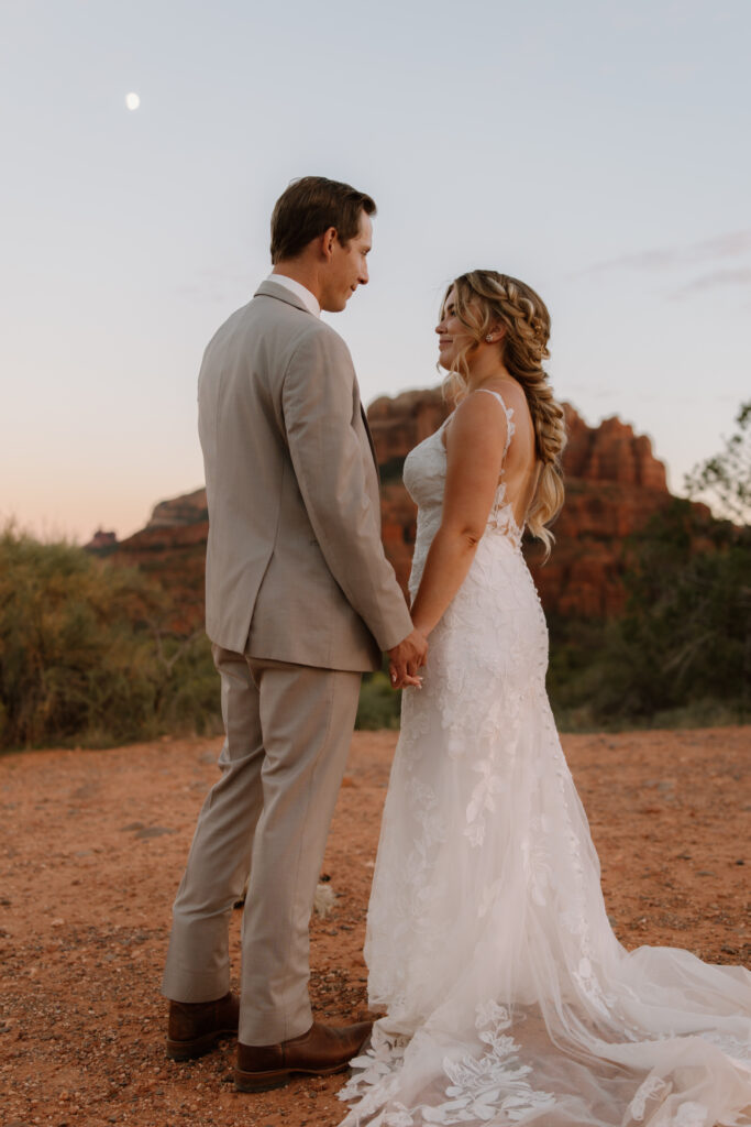 Bride and groom holding hands and gazing at each other with Cathedral Rock glowing behind them during their Sedona Arizona elopement