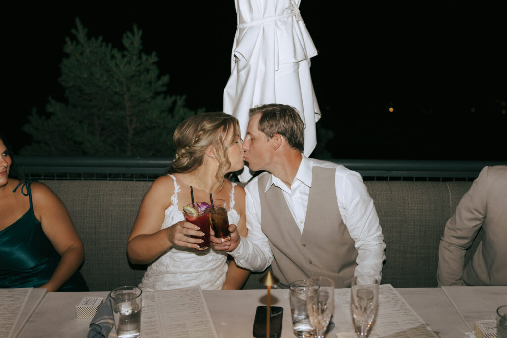 Bride and groom holding drinks and kissing at their Sedona Arizona elopement celebration dinner at Broome and Orchard