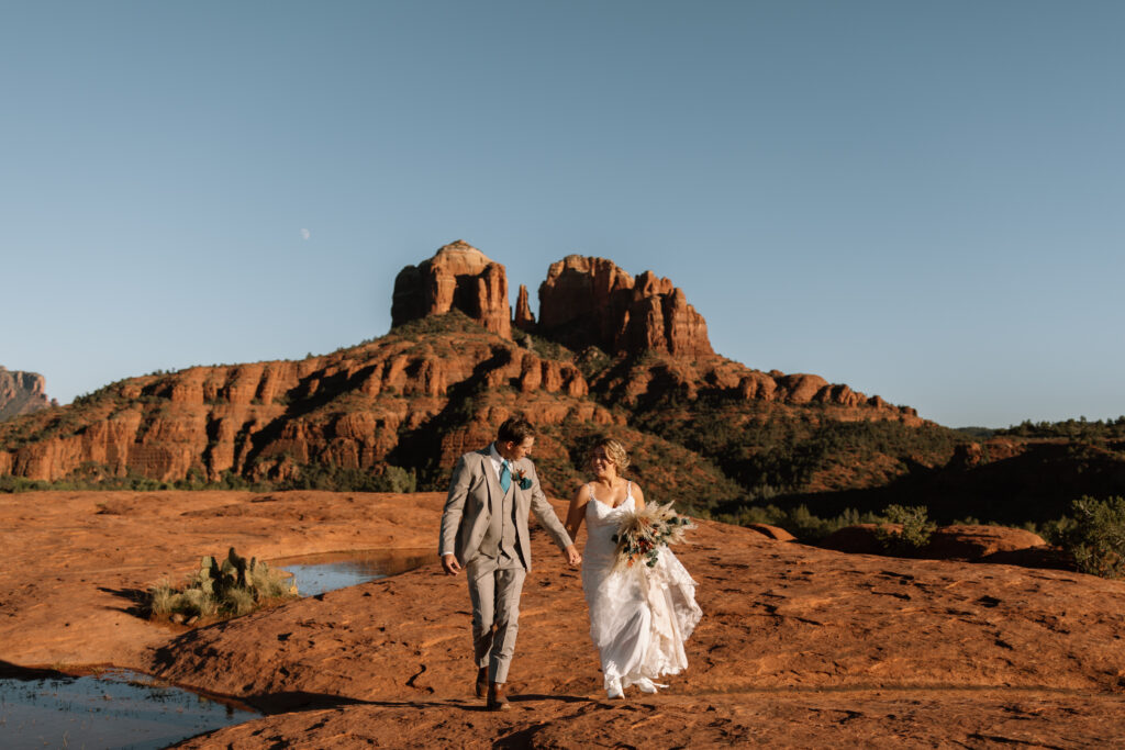Bride and groom smiling walking hand in hand away from the overlook during their Secret Slickrock elopement in Sedona Arizona