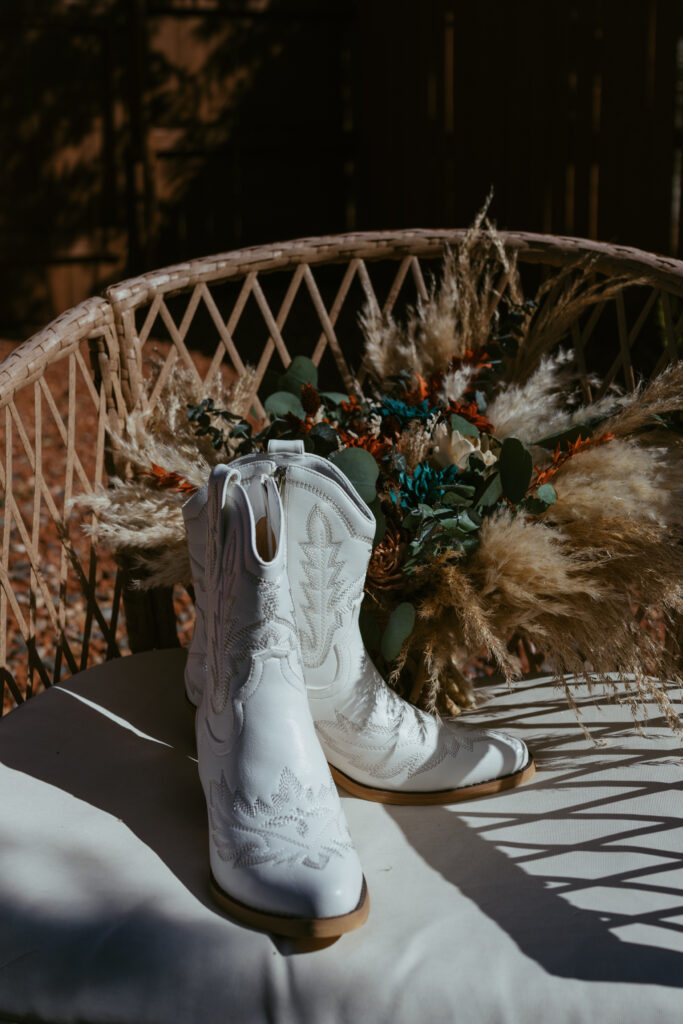 Bride's white cowgirl boots and wedding bouquet resting on a white chair during Sedona Arizona elopement getting ready details