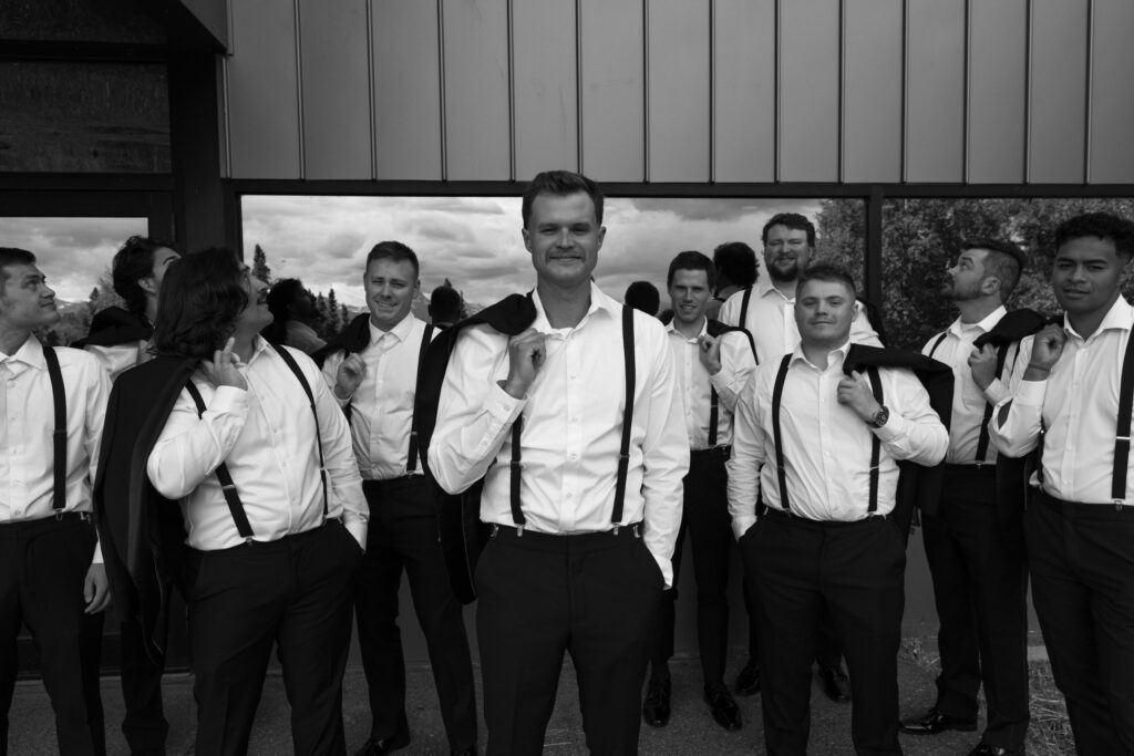 Black and white photo of groom with groomsmen in the background getting ready.