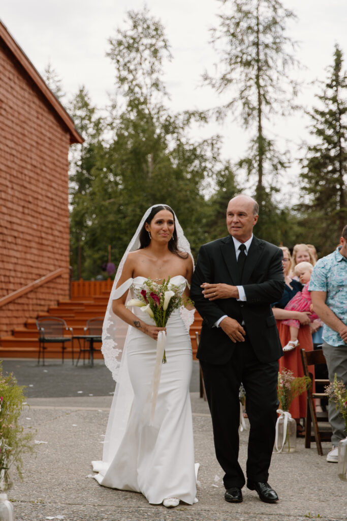 Bride walking down the aisle with her father holding back tears at their Alaska Native Heritage Center wedding in Anchorage Alaska