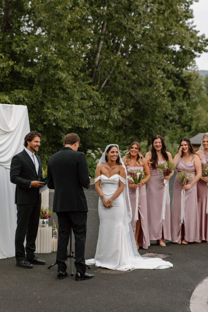 Bride laughing while looking out at guests as she and groom stand at the altar during their Alaska Native Heritage Center wedding in Anchorage Alaska