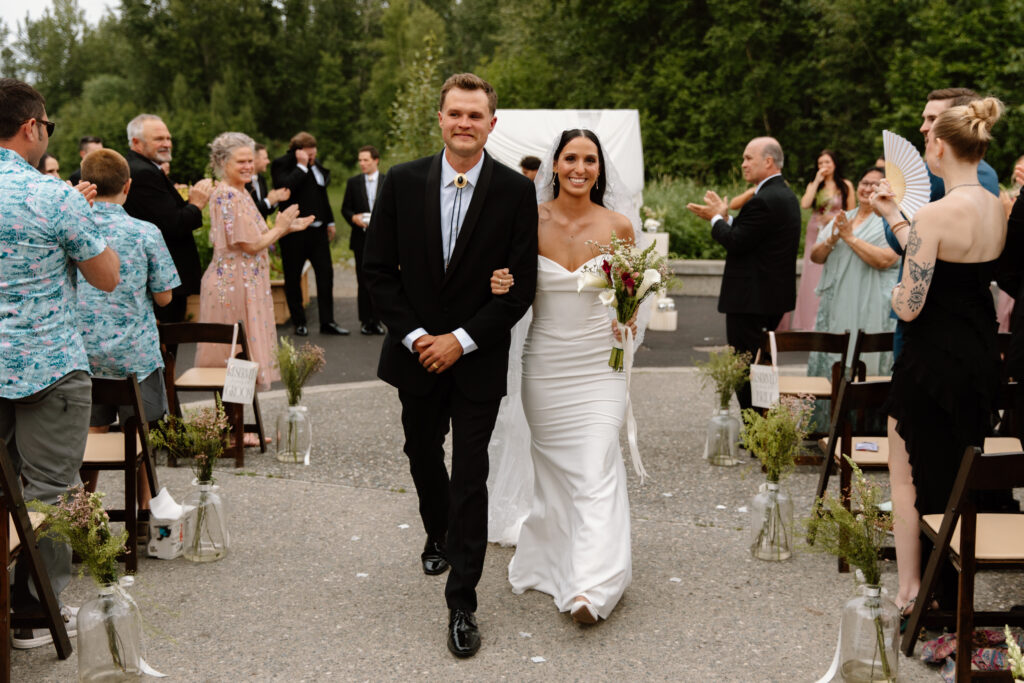 Bride and groom smiling as they walk back down the aisle after their Alaska Native Heritage Center wedding ceremony in Anchorage Alaska