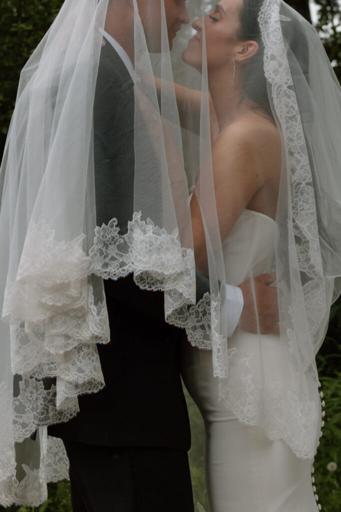 Bride and groom underneath the wedding veil about to kiss during portraits