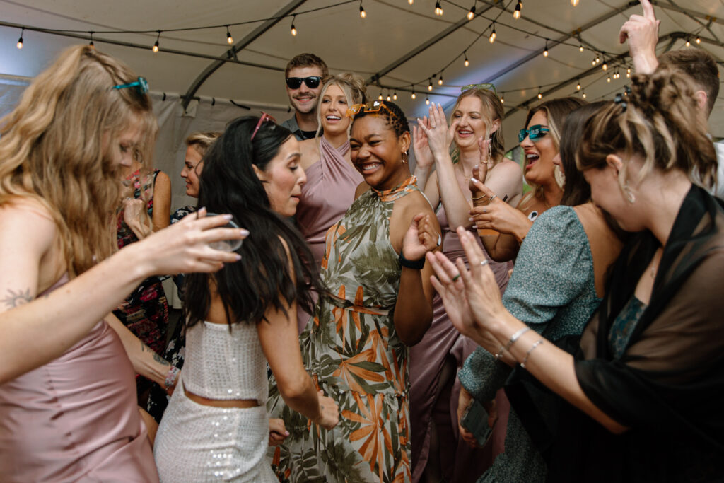 Guests smiling and dancing with the bride inside the reception tent at the Alaska Native Heritage Center wedding in Anchorage Alaska
