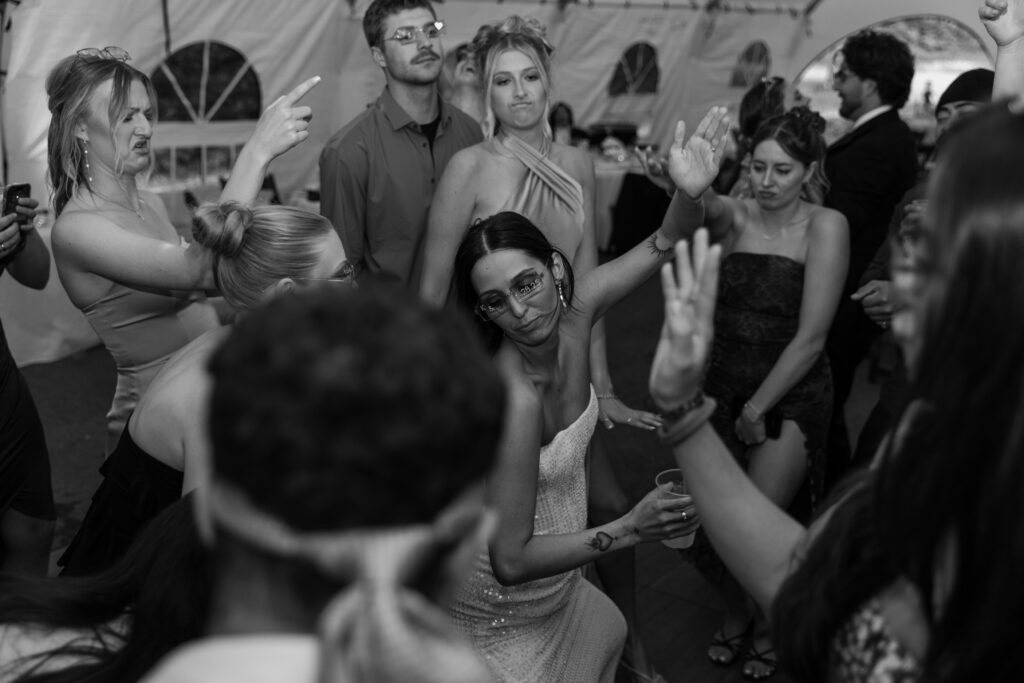 Guests smiling and dancing with the bride inside the reception tent at the Alaska Native Heritage Center wedding in Anchorage Alaska. Black and white photo.
