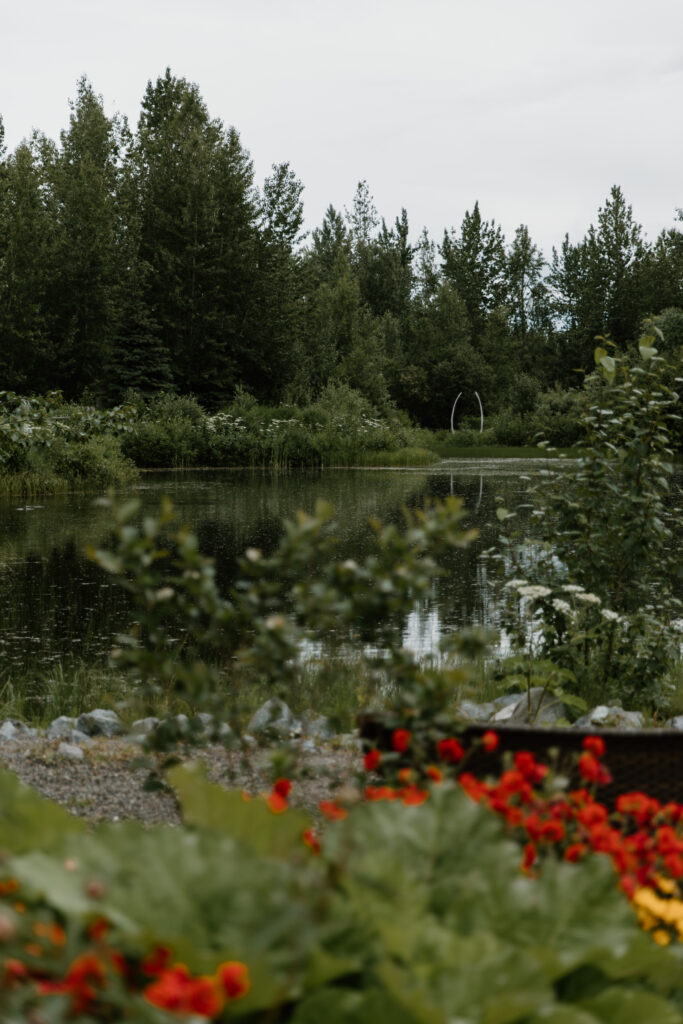 Lake view at the Alaska Native Heritage Center in Anchorage Alaska with red flowers in the foreground and a whale bone arch on the opposite shore