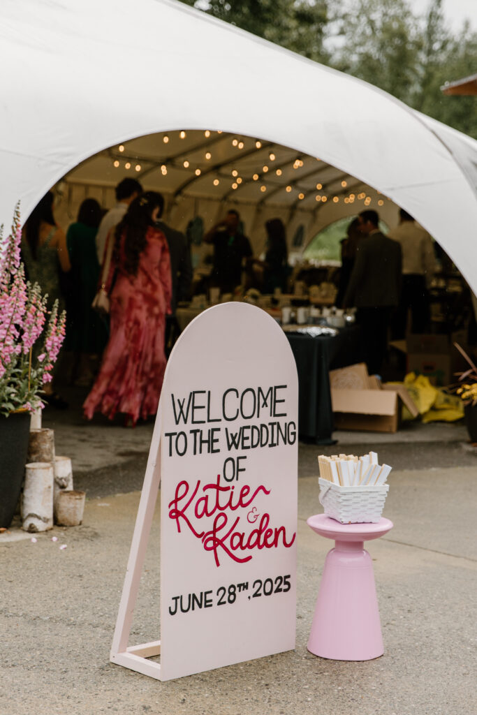 Arched wedding welcome sign with reception tent in the background at an Alaska Native Heritage Center wedding in Anchorage Alaska