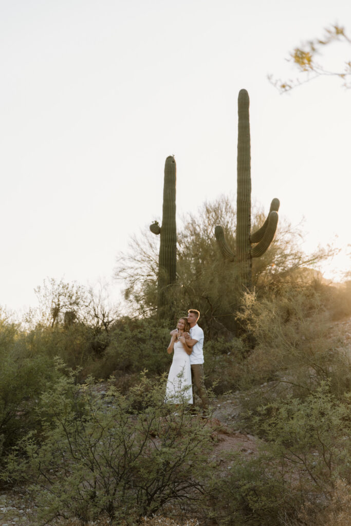 Couple embracing and looking out while standing on a rock surrounded by saguaro cacti at the Salt River