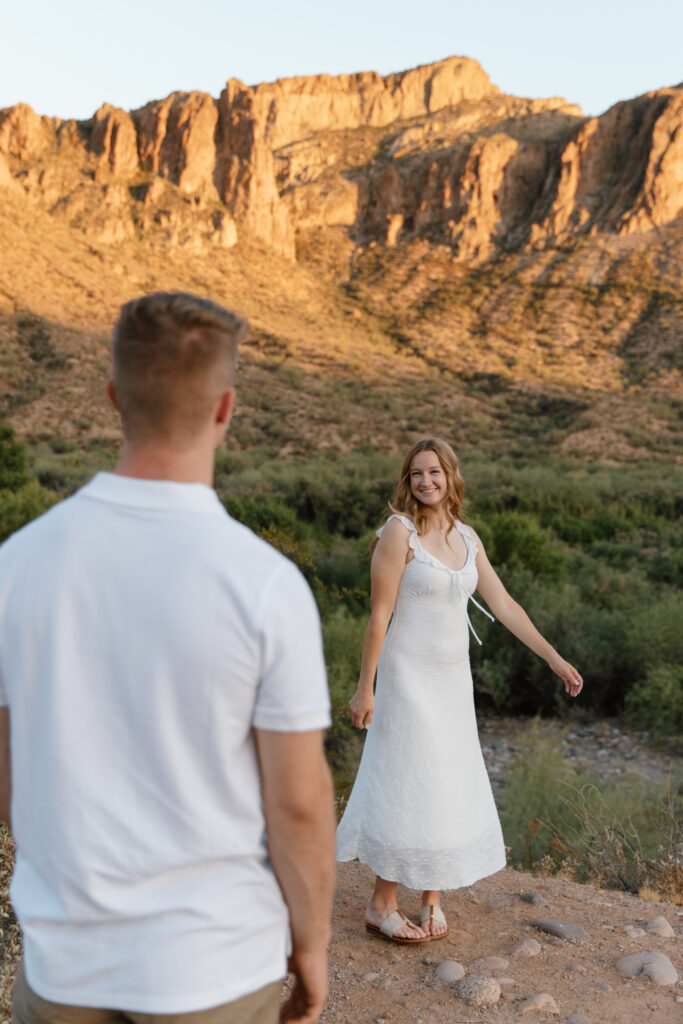 Guy watching girlfriend twirl with mountains in the background at the Salt River Arizona