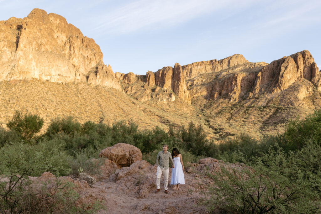 Couple walking down a hill with desert mountains in the distance during a Salt River engagement session